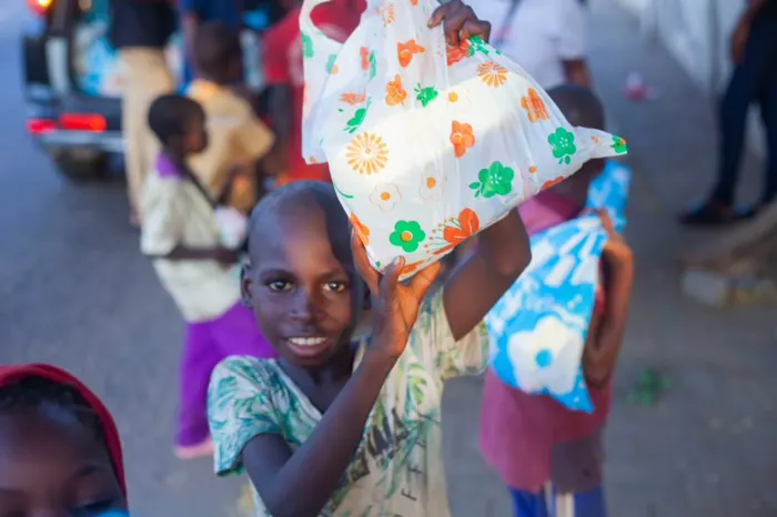 A young boy smiling as he lifts a food pack above his head