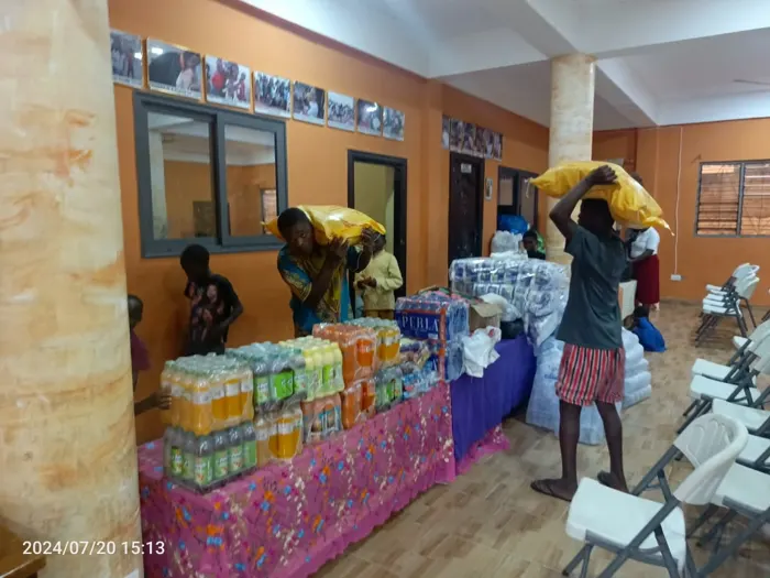 Residents carrying sacks of rice past tables stacked with drinks and bottled water