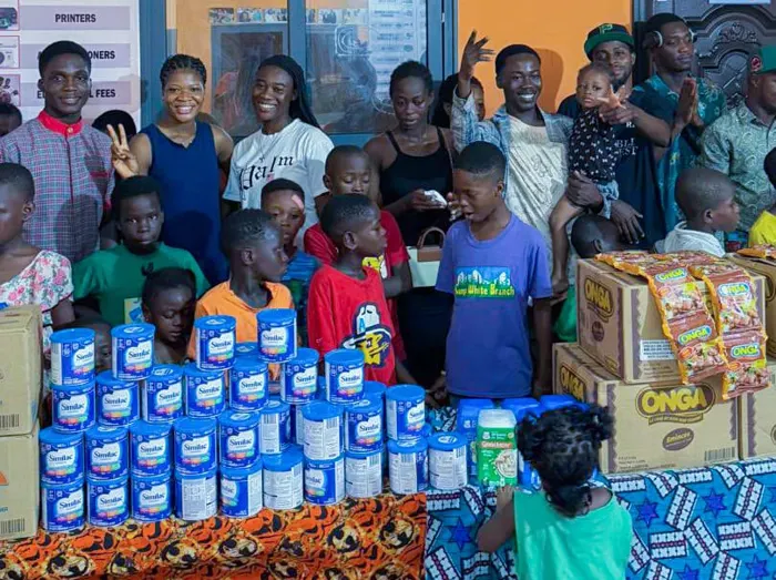 Children and ministry members behind tables stacked with tins of baby formula and cartons of noodles