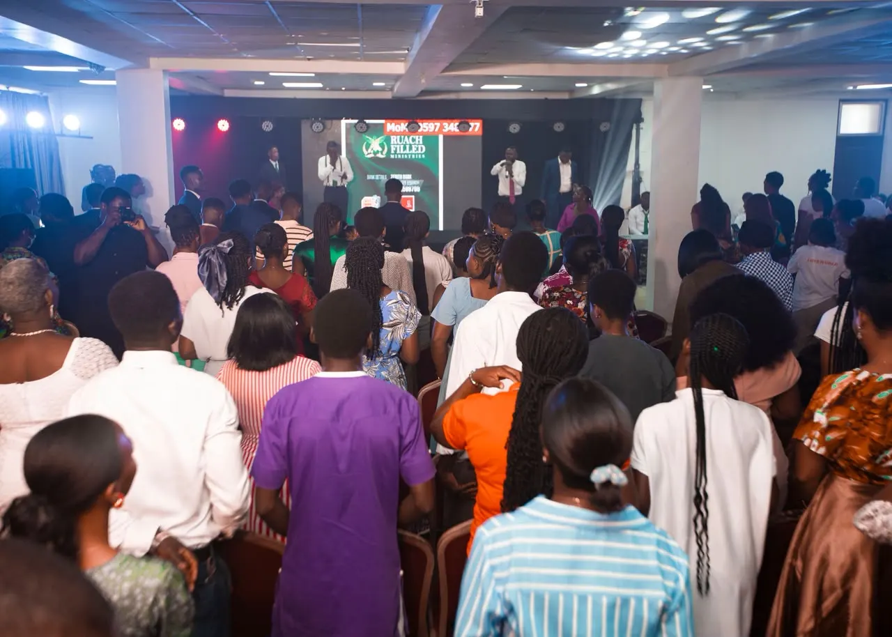 A packed conference hall standing in worship facing a stage with ministers and a Ruach Filled Ministries screen