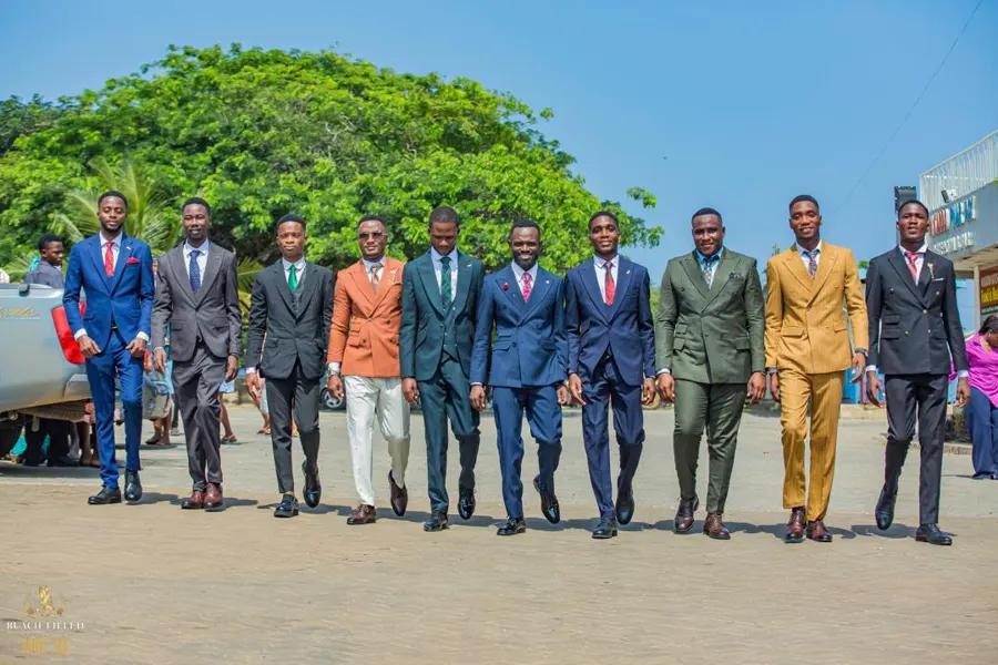 A line of young men in sharp suits walking together across the forecourt
