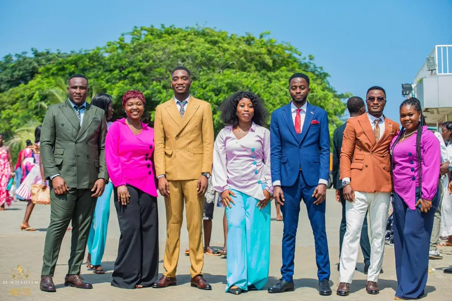 Men in suits and women in coordinated pink and lilac outfits posing together outdoors